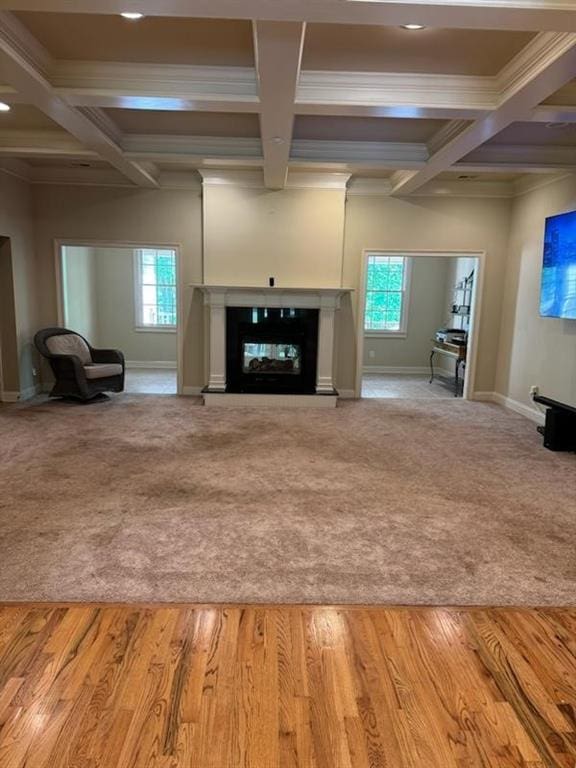 unfurnished living room with beam ceiling, light colored carpet, ornamental molding, and coffered ceiling