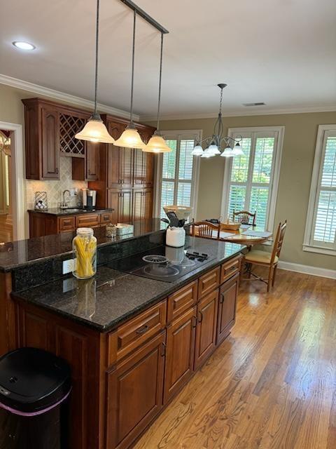 kitchen featuring ornamental molding, pendant lighting, a chandelier, a center island, and light hardwood / wood-style floors