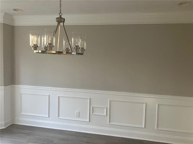 unfurnished dining area with a wainscoted wall, an inviting chandelier, wood finished floors, and ornamental molding