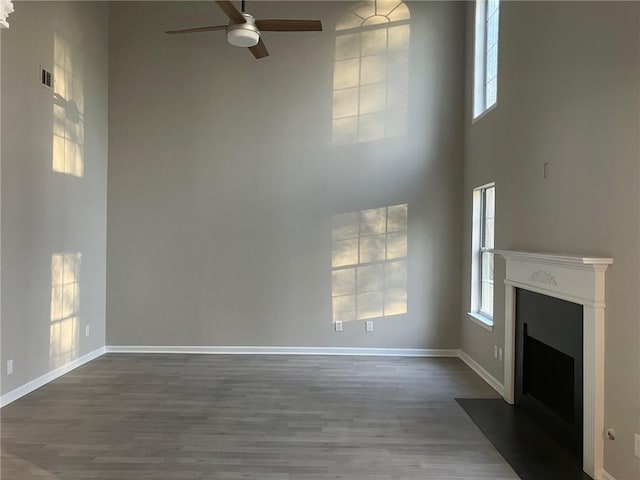 unfurnished living room featuring a fireplace with flush hearth, dark wood-style floors, a high ceiling, baseboards, and ceiling fan