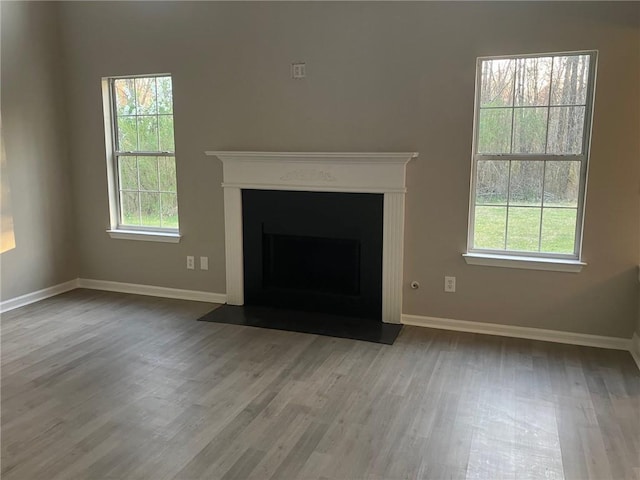 unfurnished living room featuring baseboards, wood finished floors, and a fireplace with flush hearth