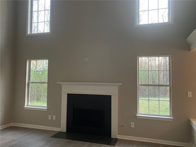 unfurnished living room featuring a fireplace with flush hearth, baseboards, wood finished floors, and a towering ceiling