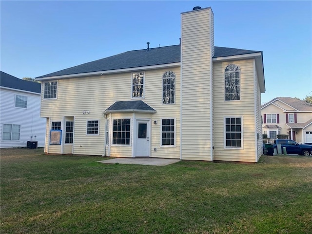 rear view of property with a patio, central AC unit, roof with shingles, a yard, and a chimney