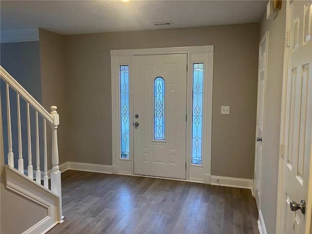 foyer featuring visible vents, baseboards, dark wood finished floors, and stairs