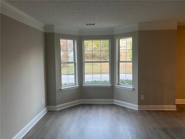 empty room with visible vents, plenty of natural light, crown molding, and wood finished floors