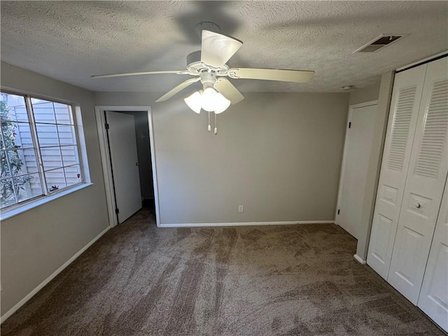 unfurnished bedroom featuring ceiling fan, dark carpet, a textured ceiling, and a closet