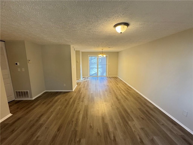 empty room featuring a chandelier, a textured ceiling, and dark hardwood / wood-style flooring