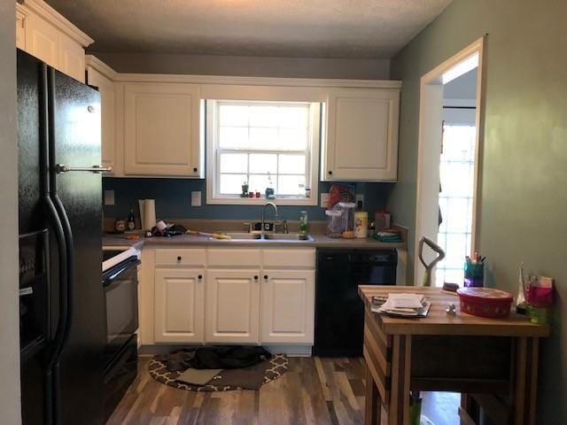 kitchen with hardwood / wood-style floors, white cabinetry, sink, and black appliances