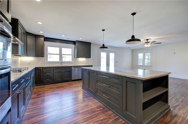 kitchen with appliances with stainless steel finishes, ceiling fan, pendant lighting, dark hardwood / wood-style floors, and a kitchen island