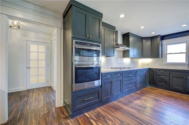 kitchen with decorative backsplash, dark hardwood / wood-style flooring, wall chimney range hood, and appliances with stainless steel finishes