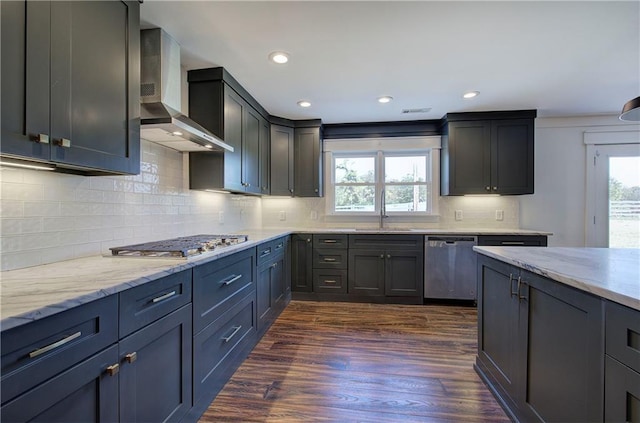 kitchen with sink, dark wood-type flooring, stainless steel appliances, wall chimney range hood, and backsplash