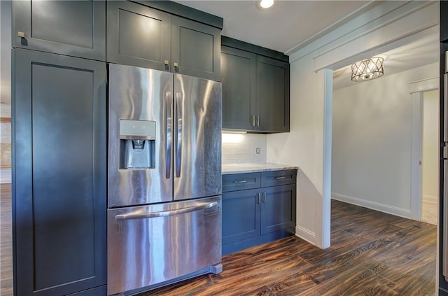 kitchen with light stone countertops, decorative backsplash, stainless steel fridge, and dark wood-type flooring