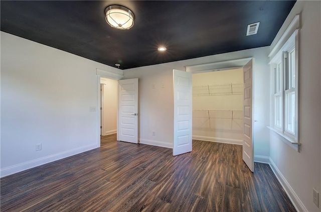 unfurnished bedroom featuring a spacious closet, a closet, and dark hardwood / wood-style floors