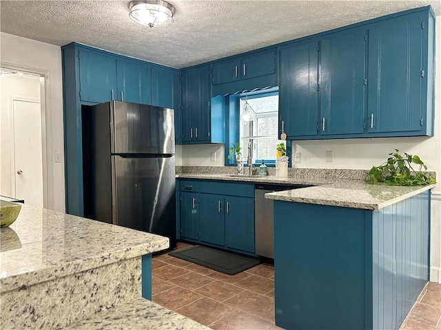 kitchen featuring blue cabinetry, sink, light stone counters, a textured ceiling, and stainless steel appliances