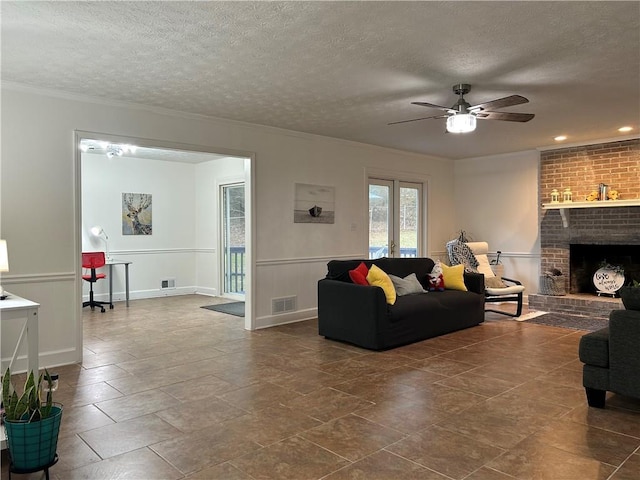 living room with ceiling fan, a brick fireplace, crown molding, and a textured ceiling