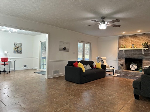 living room featuring ceiling fan, a fireplace, ornamental molding, and a textured ceiling