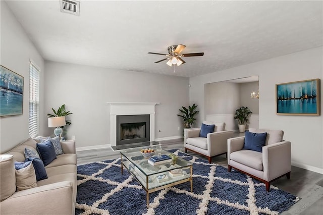 living area with wood finished floors, ceiling fan, baseboards, and a fireplace with raised hearth