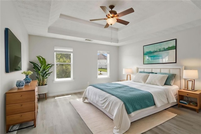 bedroom with a tray ceiling, wood finished floors, baseboards, and ceiling fan
