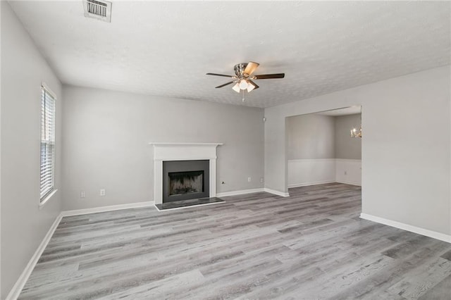 unfurnished living room featuring wood finished floors, a fireplace, a ceiling fan, a textured ceiling, and a chandelier