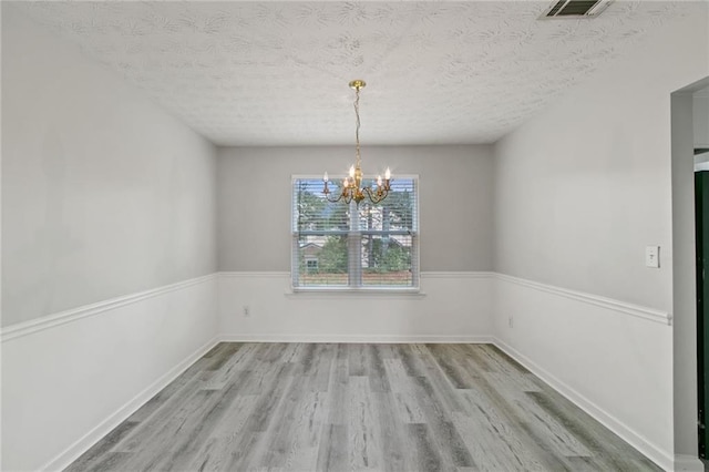 unfurnished dining area featuring wood finished floors, a chandelier, and a textured ceiling