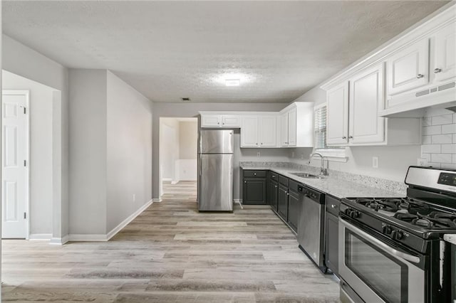 kitchen with appliances with stainless steel finishes, under cabinet range hood, a sink, white cabinetry, and light wood-style floors