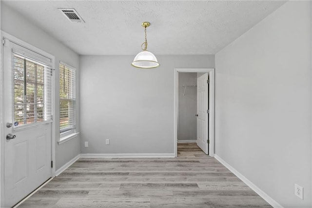 unfurnished dining area with light wood finished floors, a textured ceiling, and baseboards