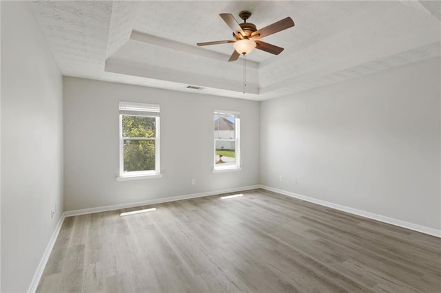 empty room featuring a raised ceiling, wood finished floors, baseboards, and ceiling fan