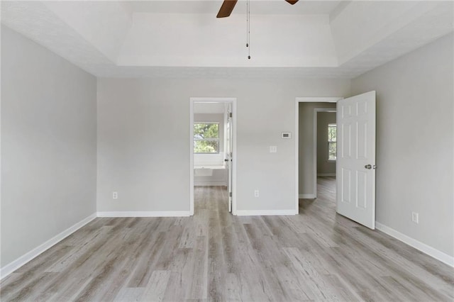 empty room featuring a raised ceiling, light wood-style flooring, and a ceiling fan