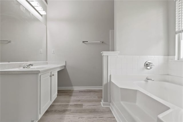full bathroom featuring wood finished floors, a garden tub, vanity, and baseboards