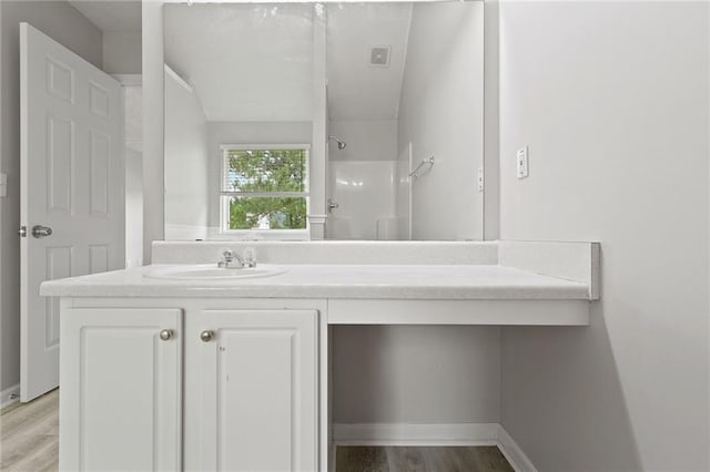 bathroom with a shower, vanity, wood finished floors, and baseboards