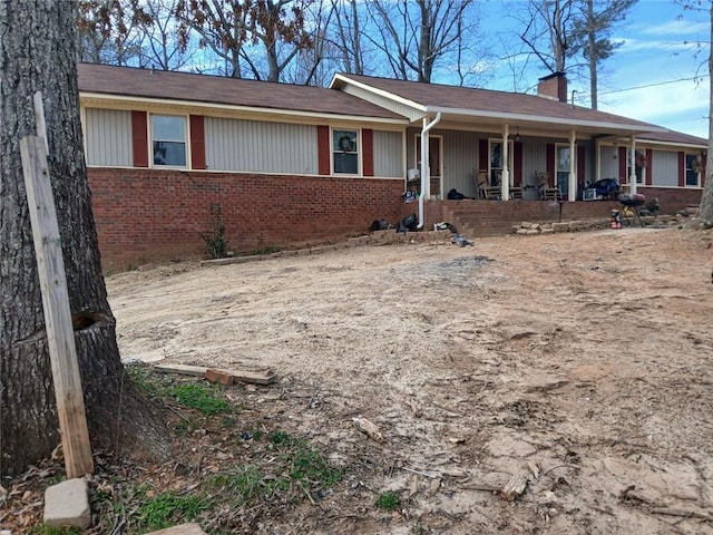 ranch-style home featuring brick siding, a chimney, and a porch