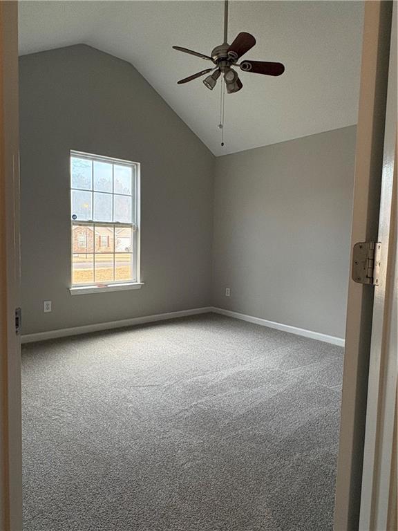 carpeted spare room with ceiling fan and vaulted ceiling