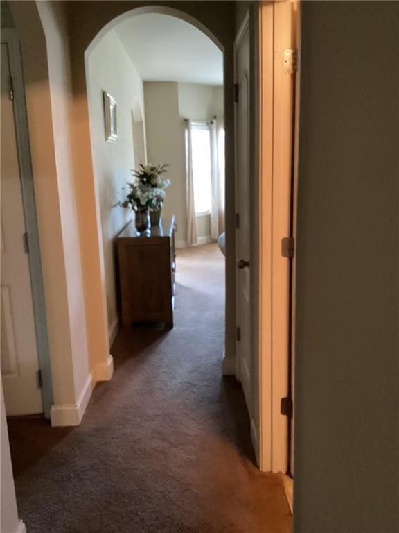 corridor with carpet flooring, arched walkways, and baseboards