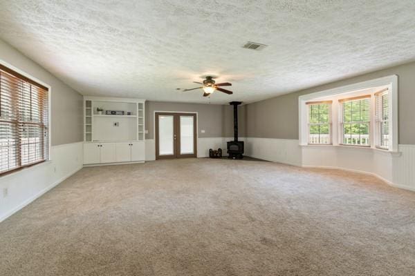 4841 Partee Trl, Social Circle, GA 30025 - unfurnished living room with a wood stove, a textured ceiling, wainscoting, ceiling fan, and light carpet