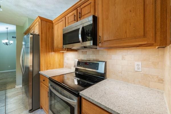 4841 Partee Trl, Social Circle, GA 30025 - kitchen featuring appliances with stainless steel finishes, a chandelier, brown cabinets, and tasteful backsplash