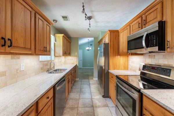 4841 Partee Trl, Social Circle, GA 30025 - kitchen with appliances with stainless steel finishes, brown cabinets, backsplash, and a chandelier