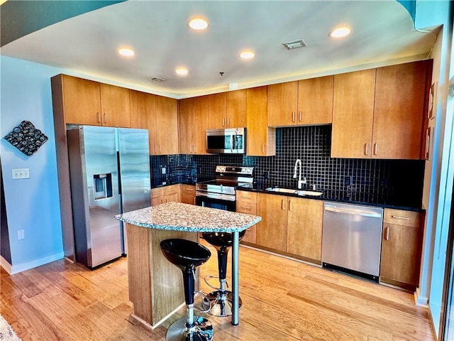 kitchen featuring stainless steel appliances, a sink, backsplash, and light wood finished floors