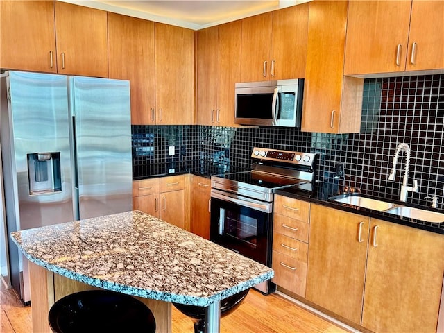 kitchen featuring dark stone countertops, decorative backsplash, stainless steel appliances, and a sink