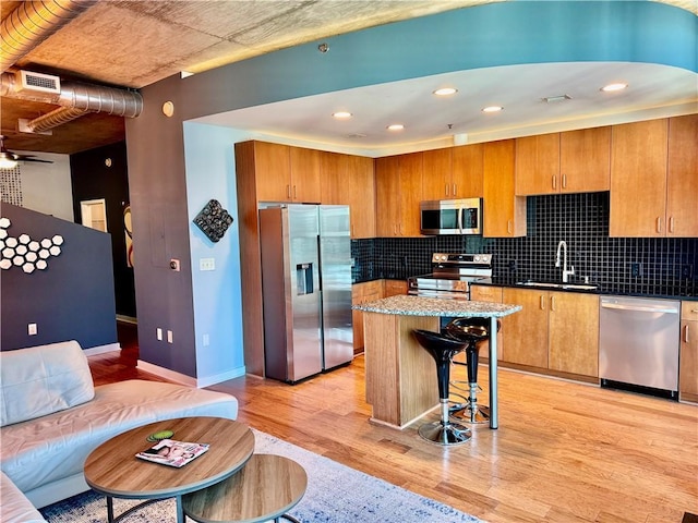 kitchen featuring light wood-style flooring, a breakfast bar, a sink, appliances with stainless steel finishes, and backsplash