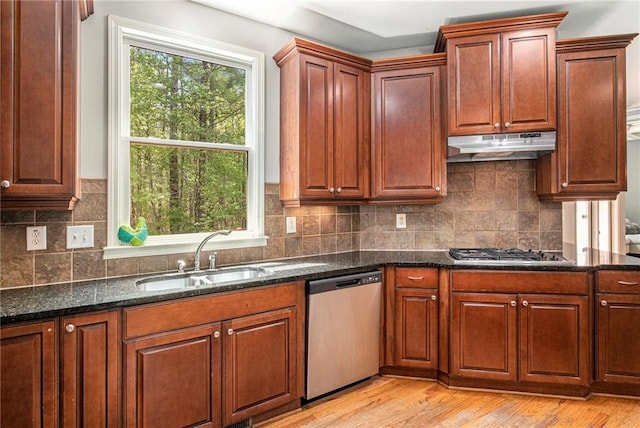 kitchen featuring light wood-style flooring, under cabinet range hood, dark stone counters, appliances with stainless steel finishes, and a sink