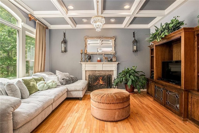living room featuring beamed ceiling, light wood-type flooring, a warm lit fireplace, coffered ceiling, and a notable chandelier