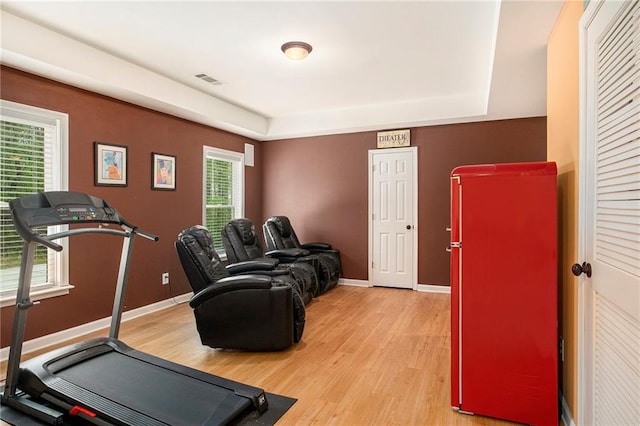 exercise room featuring visible vents, baseboards, light wood-type flooring, and a raised ceiling