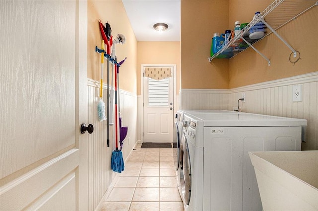 laundry area featuring light tile patterned floors, a sink, washer and clothes dryer, laundry area, and a wainscoted wall