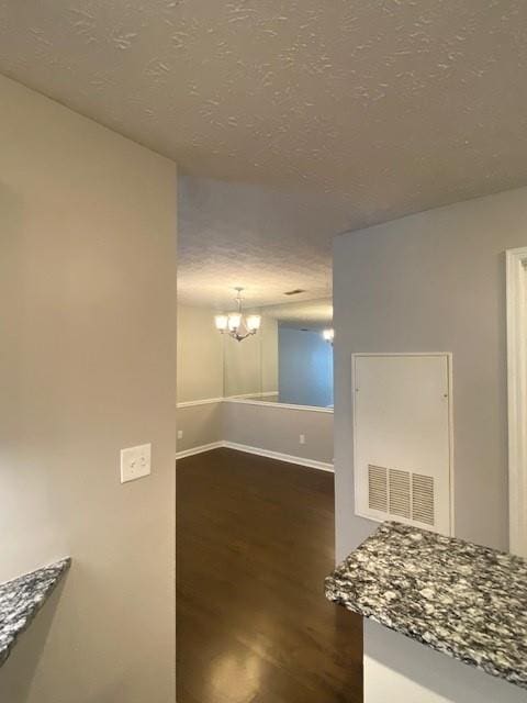 interior space featuring baseboards, visible vents, dark wood finished floors, a textured ceiling, and a notable chandelier