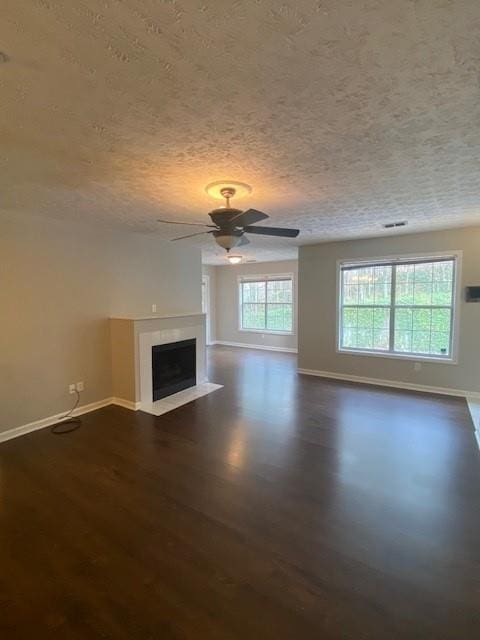 unfurnished living room with a fireplace with flush hearth, dark wood finished floors, a textured ceiling, and baseboards