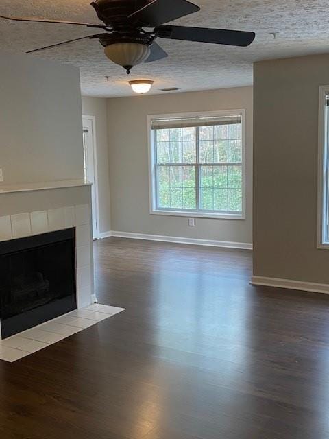 unfurnished living room with dark wood-style floors, baseboards, a textured ceiling, and a tiled fireplace