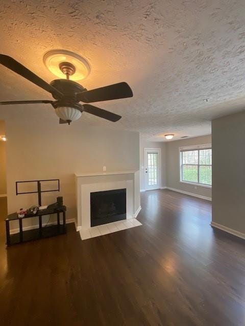 unfurnished living room featuring a fireplace with flush hearth, a textured ceiling, baseboards, and wood finished floors