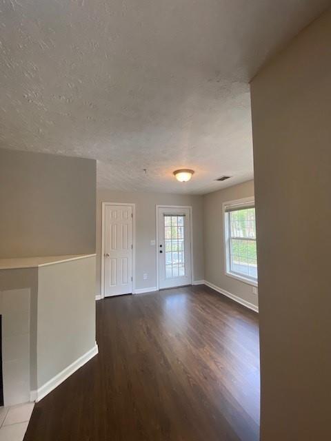 unfurnished room featuring visible vents, a textured ceiling, baseboards, and wood finished floors