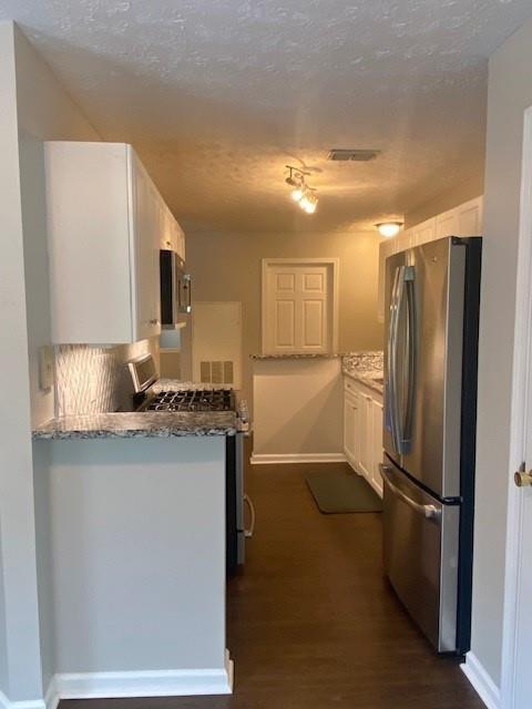 kitchen with stone counters, dark wood-style flooring, appliances with stainless steel finishes, white cabinets, and a textured ceiling