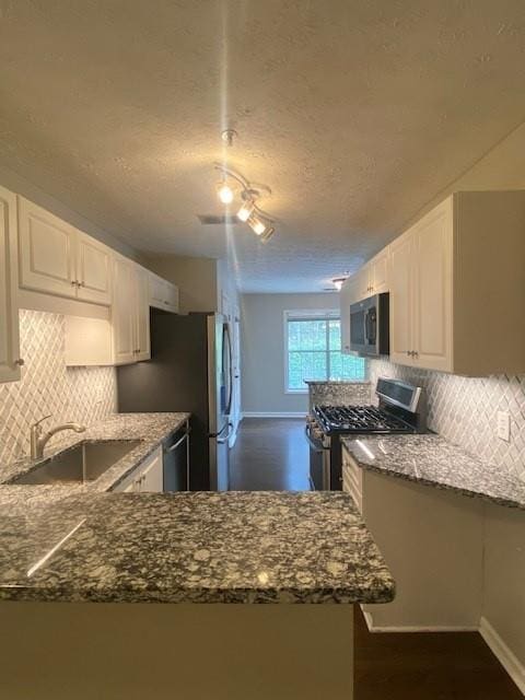 kitchen with dark stone counters, stainless steel appliances, a sink, and white cabinetry